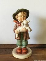 Front view of the Goebel Hummel figurine showing the boy holding the lamb, his facial features, hat, and clothing details.