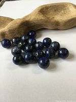 Photo showing about 20 round Lapis Lazuli beads with visible drilled holes, placed on a beige textured surface.