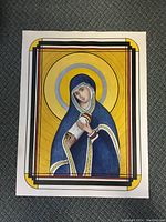 Full view of unframed religious painting of Virgin Mary with golden halo and scroll, showing bold geometric border and color.
