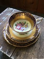 Full set photo showing tea cup stacked inside the saucer on a rustic wooden surface, highlighting the exterior rim gold designs and floral pattern inside the cup.