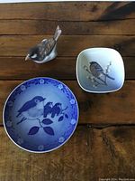 Two porcelain wall hanging plates and one porcelain sparrow ornament displayed on wooden surface