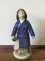 Front view of Royal Copenhagen porcelain boy figure featuring blue coat, black hair, holding salmon fish, standing on textured base.