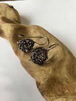 Pair of silver drop earrings shown on carved wood background, visible ornate granulated design and twisted rope border.