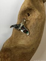 Whale tail pendant displayed on a natural wood piece, showing the abalone shell inlay with silver details.