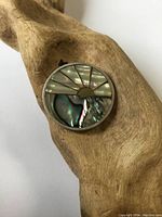 Round sterling silver pendant with abalone shell inset laid on wooden surface.