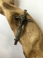 Front view of silver cross pendant featuring detailed face of Christ and rectangular shape resting on wooden surface.