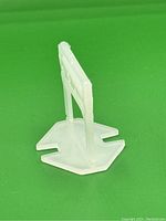 Side view of a single translucent plastic tile levelling clip showing the L shape with wings and vertical spacer.