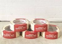 Five rolls of utility masking tape stacked in two rows, with red and white labels showing product name and measurements.