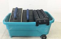 Top-down view of blue plastic bucket containing two grout floats and two black cylindrical rollers inside the bucket.