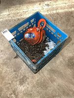 Orange 1 ton come along chain hoist with chain inside a blue plastic crate on the floor.