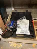 Black & Decker drill and charger inside black plastic carrying case with manual and other accessories visible.