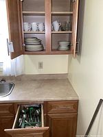 Open kitchen drawer showing green cutlery tray containing stainless steel forks, spoons, and knives.