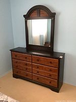 Full front view of a 6 drawer dresser with attached mirror in a bedroom corner, showing the two-tone finish and drawer arrangement.