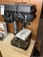 View of Jobmate drill press on a workbench, showing the upper part and table with manual on it.
