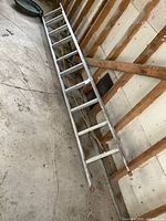 Full view of the aluminum extension ladder laid on a concrete floor next to a wooden wall.