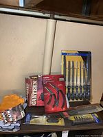 Photo showing work gloves, Husky pistol grip pliers in packaging, machinist file set in packaging, additional tools and a canteen.