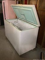White Kenmore chest freezer with lid open showing metal wire baskets inside. Basement setting with wooden walls.