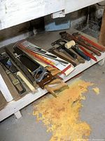 Photo shows the hand tools arranged on a shelf including saws, pipe wrenches, pry bars, and hammers.