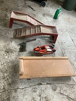 Overview of two steel auto ramps, orange hydraulic trolley jack, green bottle jack, and vintage wooden creeper on concrete floor.