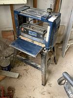 Front view of Mastercraft thickness planer on metal stand showing planer surface, control panel, and adjustment knob with sawdust residue.