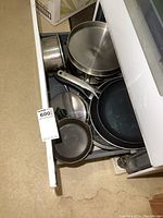 Drawer containing multiple pots and pans including stainless steel pots, non-stick frying pans, and a small cast iron pan.