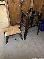 Wood router with a wooden table and attached clamp, electrical cord visible, placed on concrete floor.