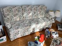 Front view of floral patterned 3-seater sofa, showing the cushioned backrests, arms, and fabric skirt around the base