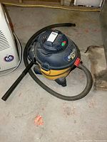 Full view of Rona 5 gallon shop vacuum showing yellow and black body, flexible hose, and floor attachment.