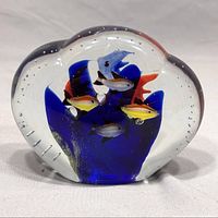 Front view of Murano style art glass paperweight showing colorful glass fish and coral inside clear glass with many small air bubbles.