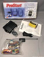 Full lot arranged on gray surface showing box, control module, remote key fob, wiring harness, antenna, and manuals.