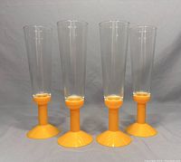 Four vintage Bodum champagne flutes with yellow plastic bases and clear glass tops shown from an angle.