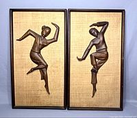 Pair of vintage carved wood dancers wall art panels side by side, framed, on beige textured background