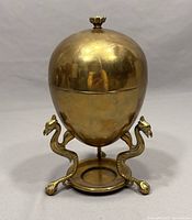 Front view of brass egg warmer showing egg shape and dragon legs.