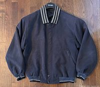 Front view of navy blue bomber jacket with checkered collar laid flat on wooden floor.