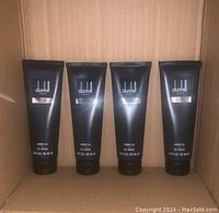 Front view of four black tubes of Dunhill London Desire Blue shower gel inside a cardboard box.