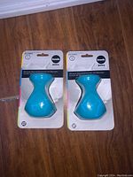 Two new blue silicone sleeves still in original packaging for Joovy Boob 8oz baby bottles, displayed on wooden floor.