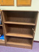 Front view of the brown wooden bookcase showing four shelves and its wood grain pattern.