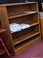 Full view of the medium-toned wooden bookcase showing 4 shelves with adjustable shelf placement, rounded top edges, and visible wood grain.