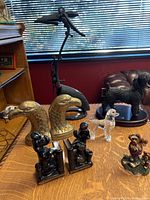 Photo showing collection of animal figurines and bookends including brass eagle heads, crystal and ceramic poodles, black Boyd Bears, painted dog figurine, and a black metal bird sculpture