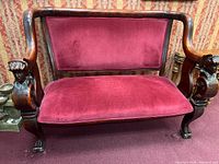 Front view of the loveseat showing dark wood frame with carved details and red velvet cushions.