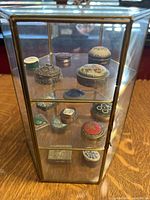Hexagonal brass and glass display case containing pillboxes on three shelves