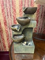 Front view of multi-tier water fountain showing four cascading bowls and pebble base.