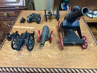 Overview of eight miniature cannons on tabletop showing various sizes and finishes