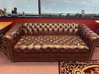 Front view of dark brown leather tufted sofa with rolled arms and nailhead trim