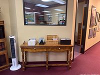 Photo of wooden library table with two drawers placed against a wall in a room with hardwood flooring and a large window reflecting ceiling lights