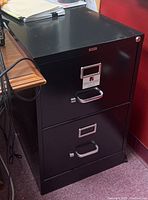 Black metal 2-drawer filing cabinet with handles, label holders, and locking mechanism on top drawer.