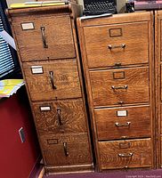 Photo showing two vertical oak filing cabinets side by side, each with four drawers and metal handles, suitable for legal files storage.