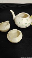 Photo showing large Belleek teapot (missing lid), cream and sugar bowl on black background highlighting shamrock decoration and overall shape