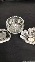 Three crystal items on black surface: elephant figurine, crystal bowl, and flower-shaped crystal clock