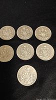 Seven Canadian fifty cent coins arranged on black fabric, showing coat of arms design.